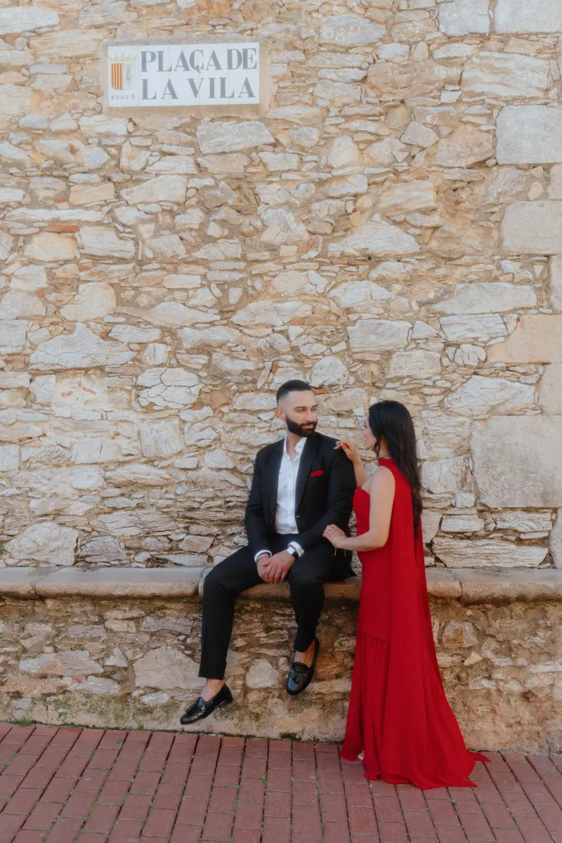 A couple shares an intimate moment by a rustic stone wall in Begur during a surprise proposal photoshoot.