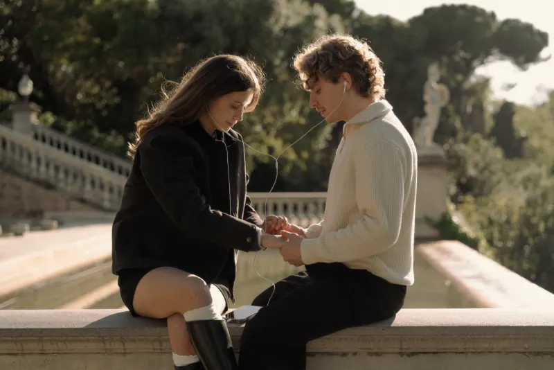 A couple shares headphones and holds hands on a sunlit terrace in Barcelona during a couples & engagements photoshoot.