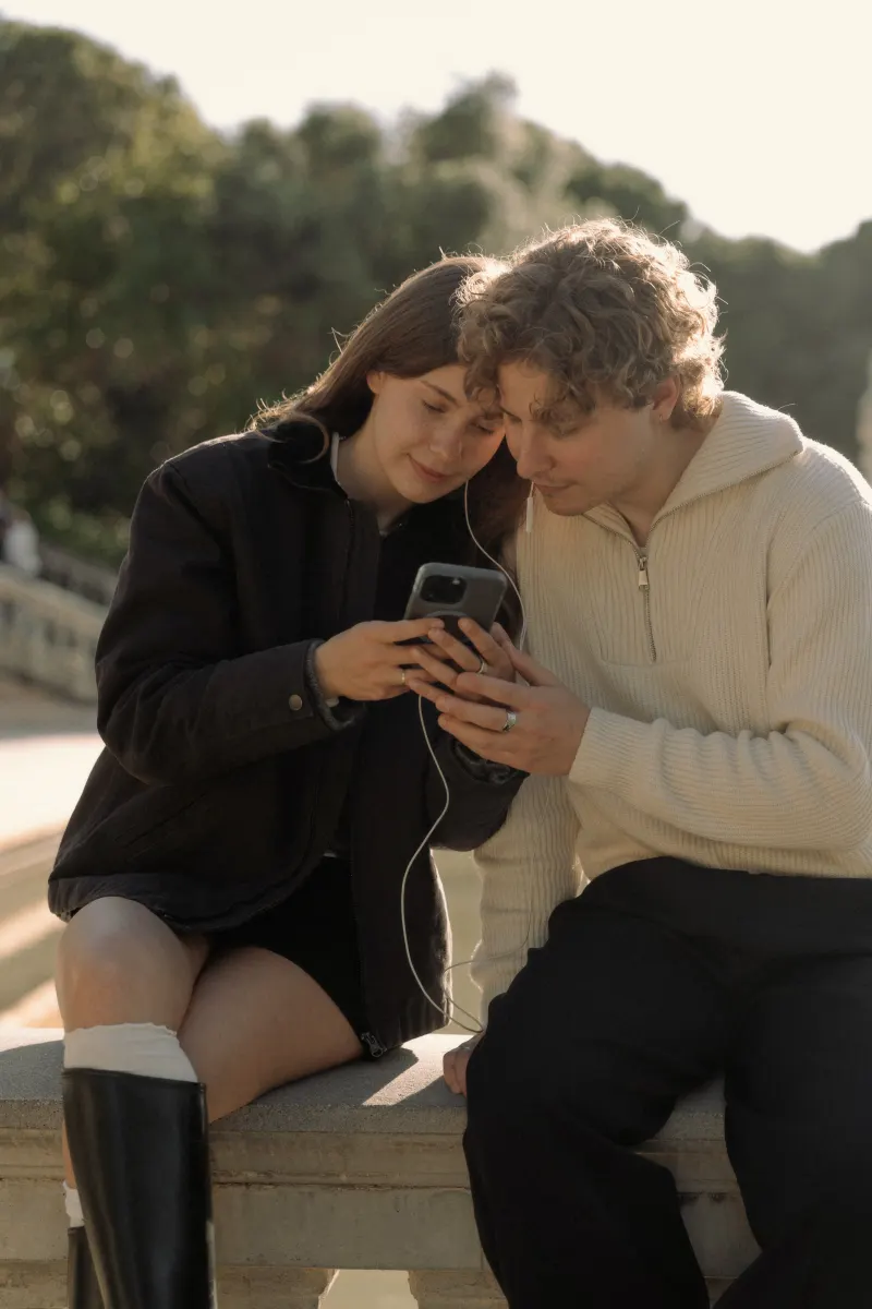 A couple shares headphones and smiles at a phone together during a relaxed couples & engagements photoshoot in Barcelona.