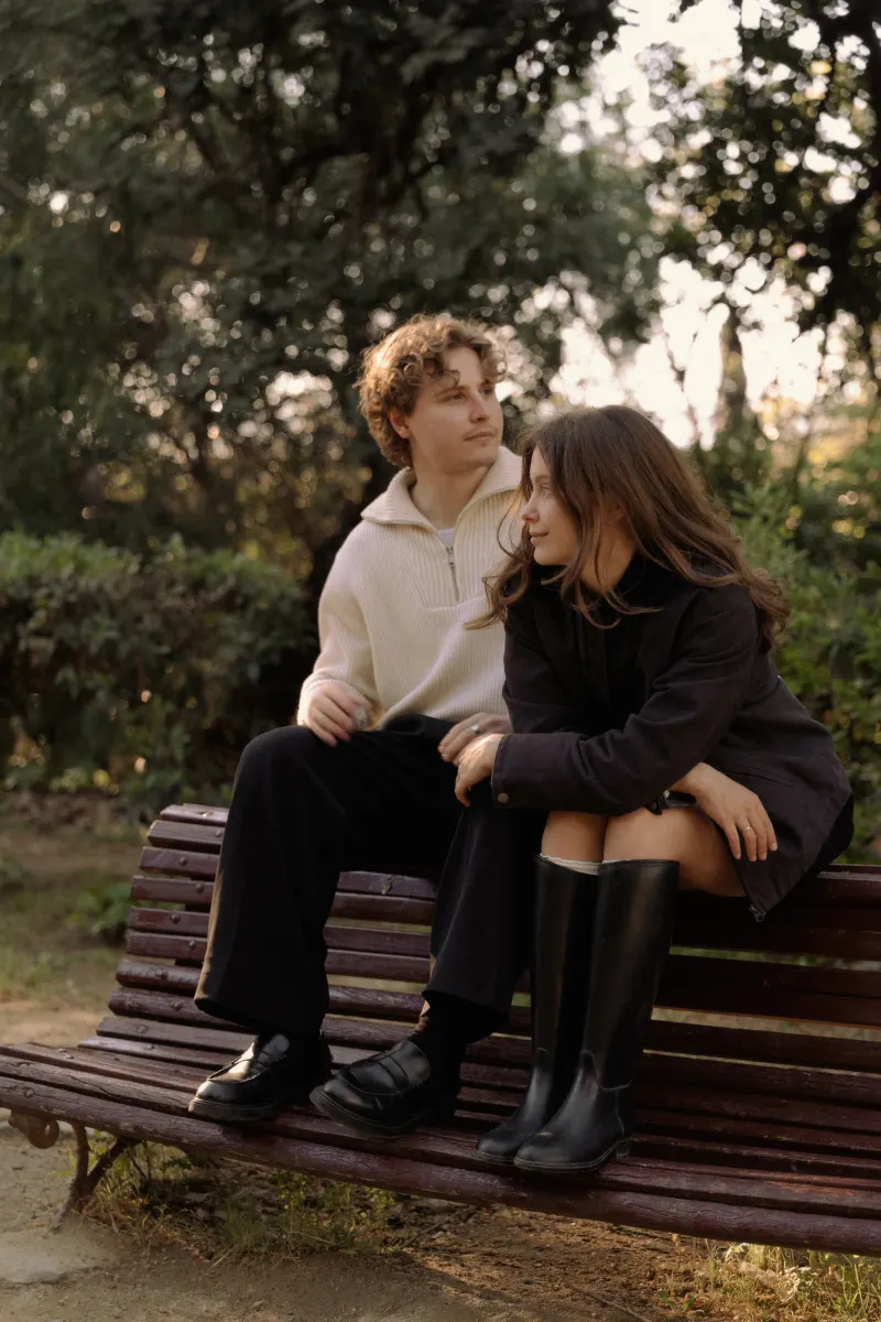 A couple sits close on a park bench in Barcelona, sharing a quiet, thoughtful moment during their engagement photoshoot.