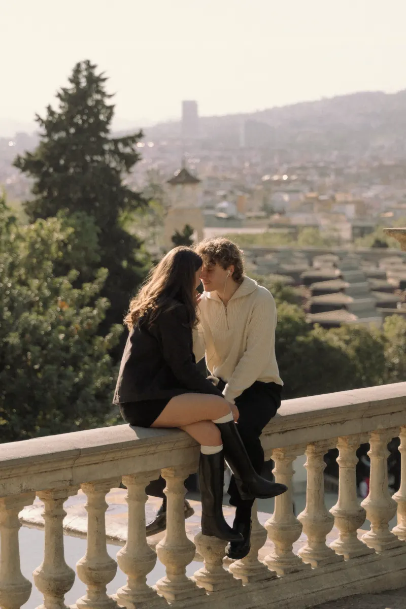 A couple sits close on a stone balcony in Barcelona, sharing headphones during a relaxed couples & engagements session.