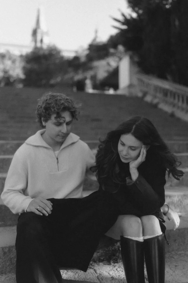 A couple sits close on stone steps in Barcelona, sharing a quiet, thoughtful moment during their engagement photoshoot.