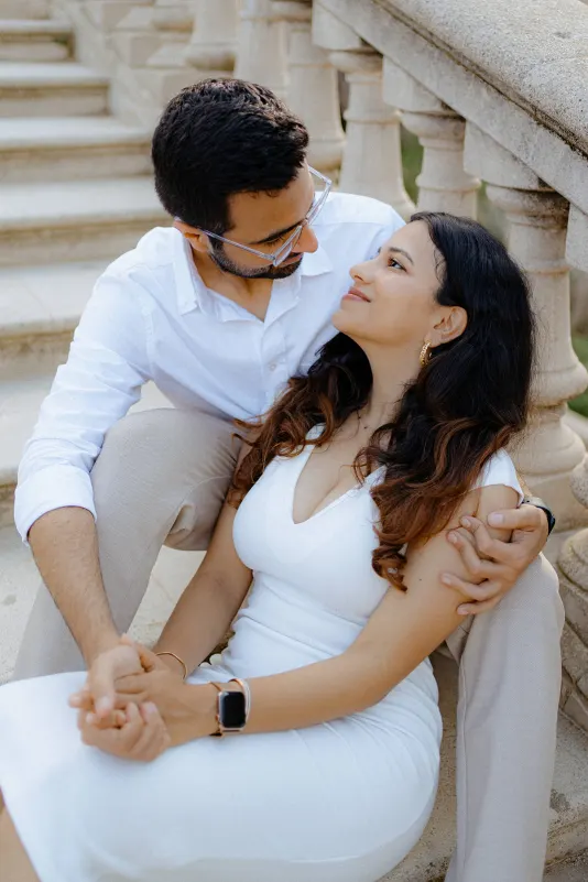 A couple sits close on stone steps, sharing a loving gaze during their surprise proposal photoshoot in Barcelona.
