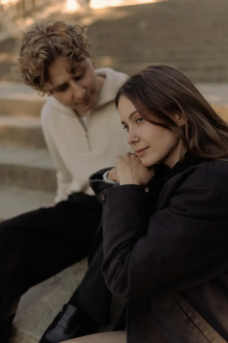 A couple sits close on sunlit steps in Barcelona, sharing a quiet, thoughtful moment during their engagement photoshoot.