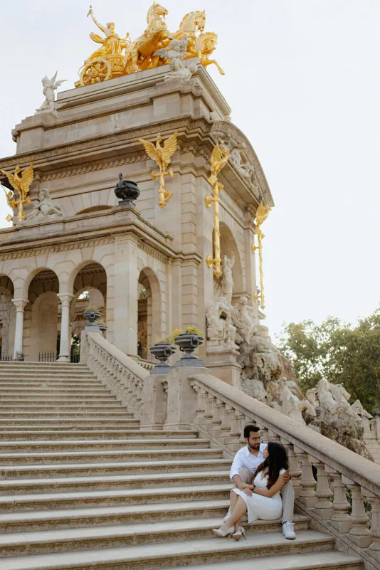 A couple sits close on the grand steps of Barcelona’s Cascada Monumental, sharing a quiet moment after a surprise proposal.