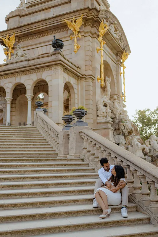 A couple sits on the steps of Parc de la Ciutadella, sharing a loving embrace during their surprise proposal photoshoot.