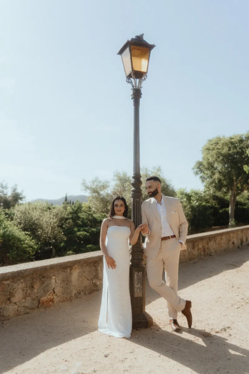 A couple stands by a vintage lamppost, sharing a quiet moment after their surprise proposal photoshoot in the sun.