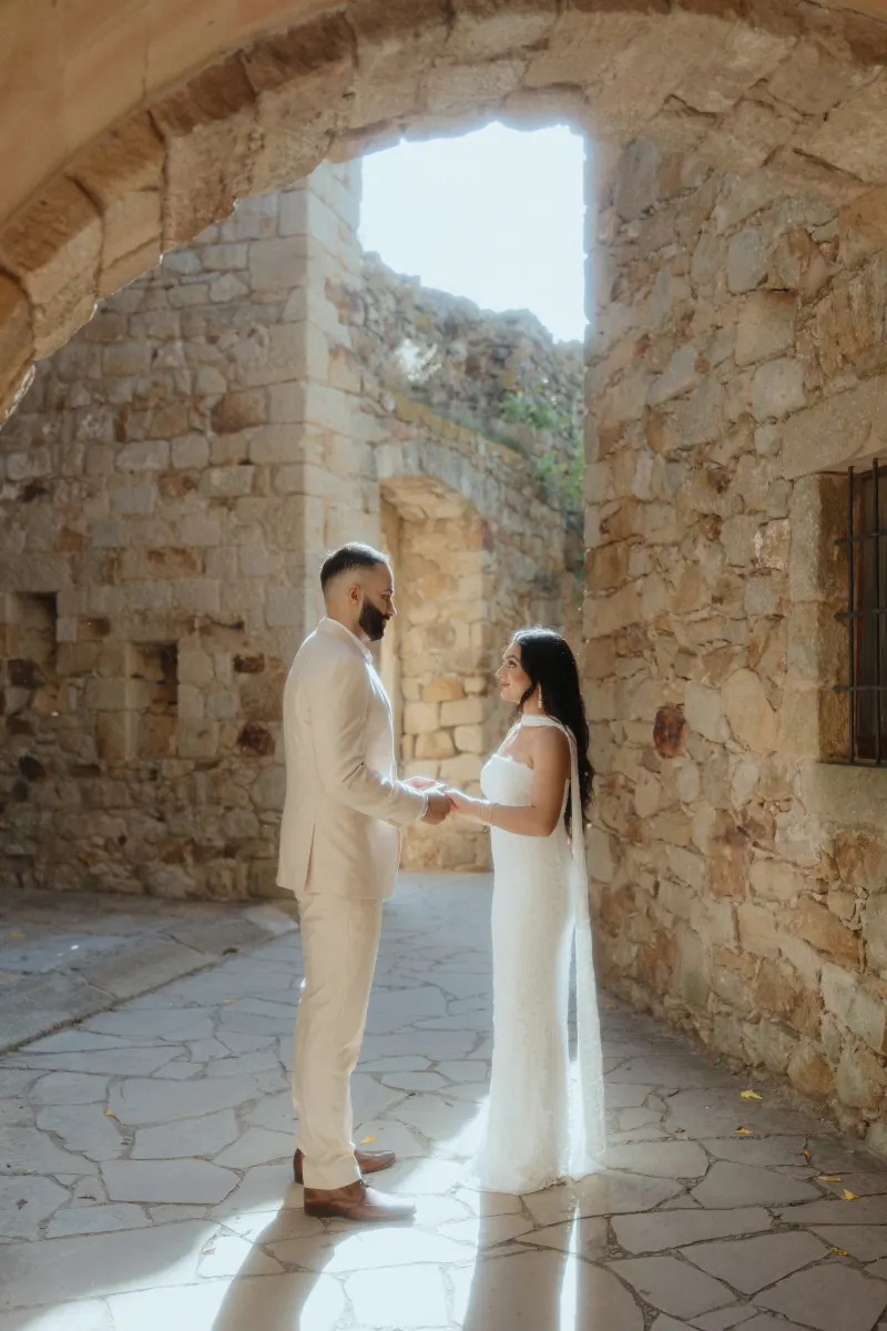 A couple stands hand in hand, sharing an emotional moment in a sunlit stone passage during their surprise proposal session.