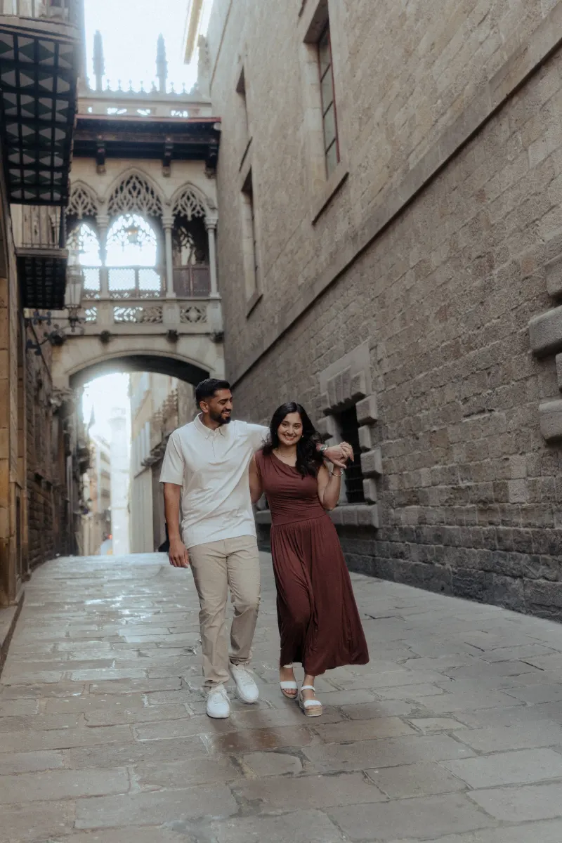 A couple strolls arm in arm, sharing a happy moment during their couples & engagements photoshoot in a historic alley.
