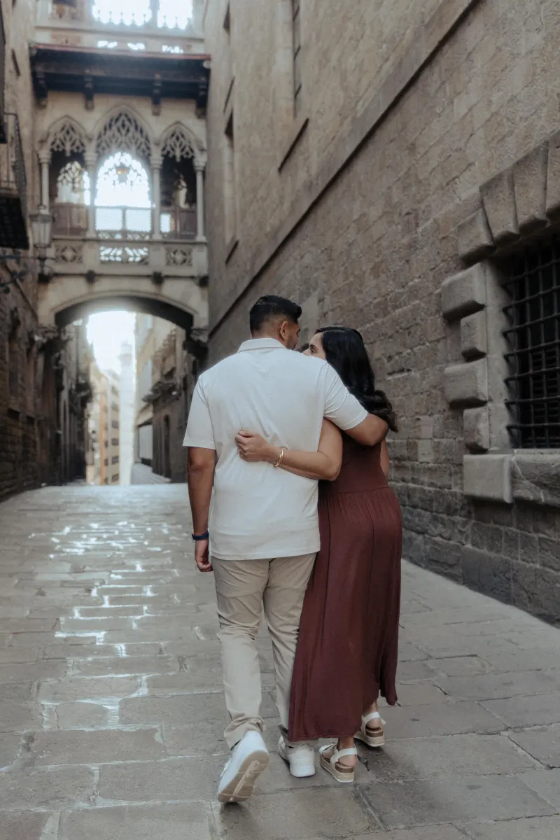 A couple walks arm in arm down a historic stone alley, sharing a quiet moment during their engagement photoshoot.