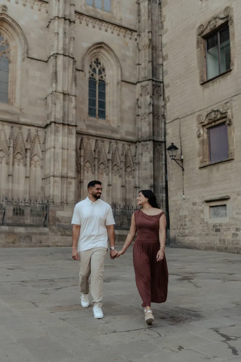 A couple walks hand in hand, sharing a joyful moment during an engagement session in a charming old city square.