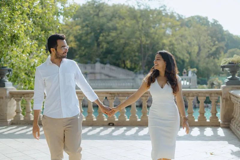 A couple walks hand in hand, smiling warmly at each other during a surprise proposal photoshoot in Parc de la Ciutadella.