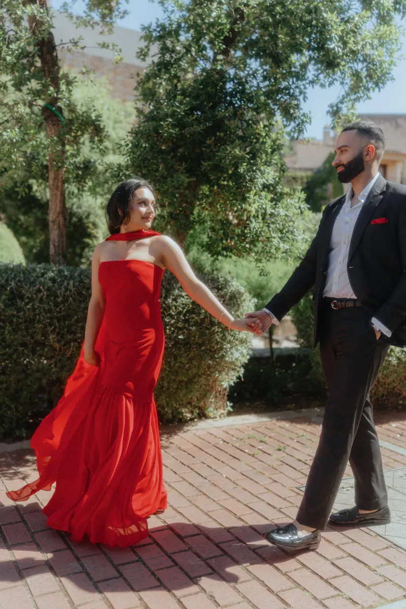 A couple walks hand in hand through a sunlit Begur garden, sharing a joyful moment during their surprise proposal shoot.