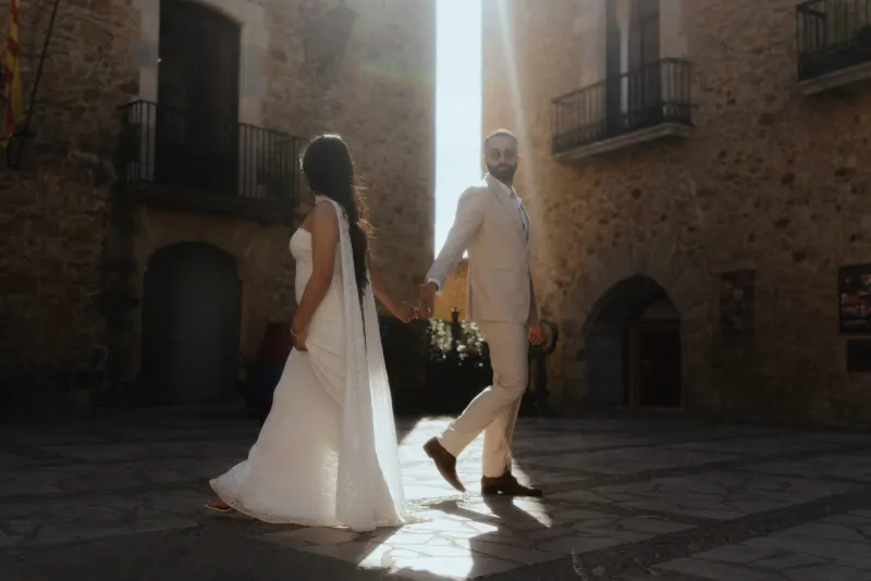 A couple walks hand in hand through a sunlit stone courtyard, captured during their surprise proposal photoshoot.