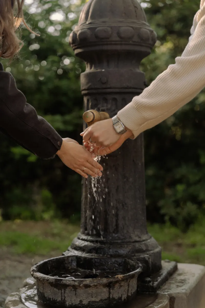 A couple washes their hands together at a park fountain in Barcelona during a candid couples & engagements photoshoot.