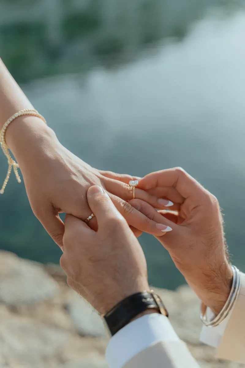 A heartfelt lakeside surprise proposal as he gently places an engagement ring on her finger.