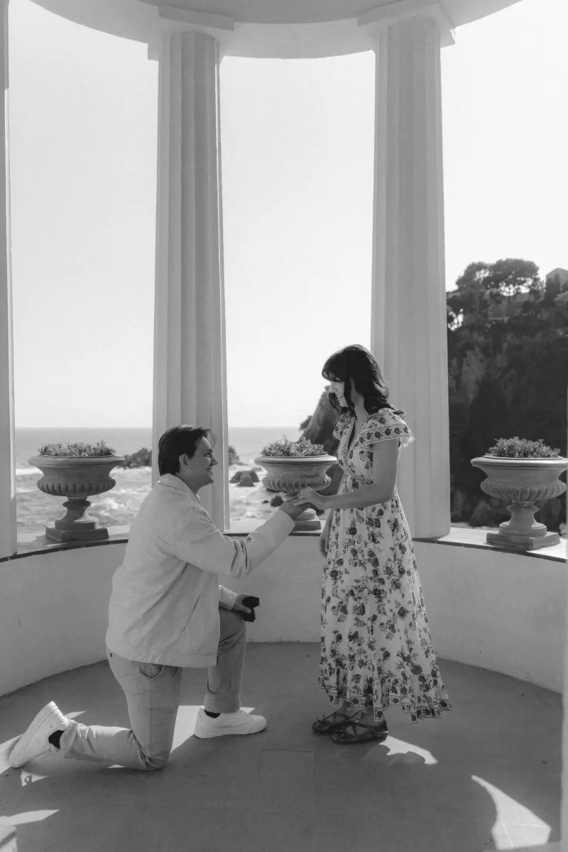 A joyful couple during a seaside surprise proposal, captured in a candid moment by professional photography.