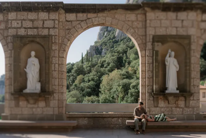 A large stone arch and carved statues frame Tim and Megan on the bench.