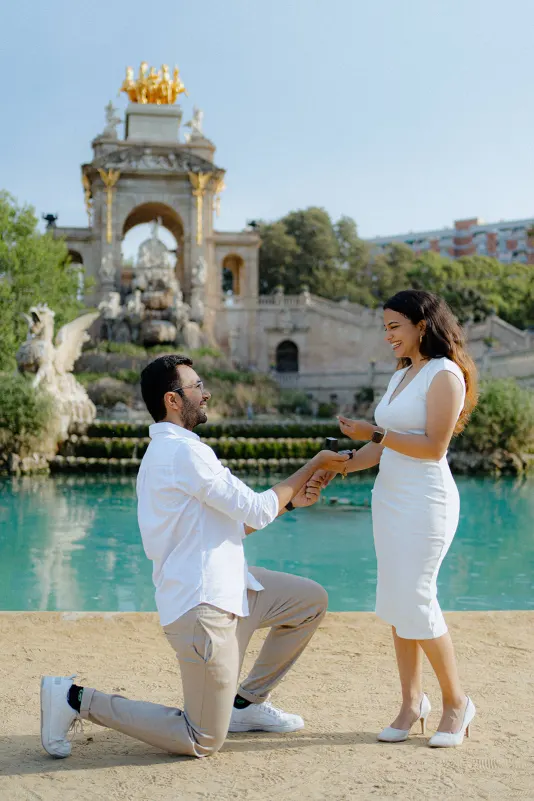 A man proposes on one knee by the fountain at Parc de la Ciutadella, capturing a joyful surprise proposal moment.