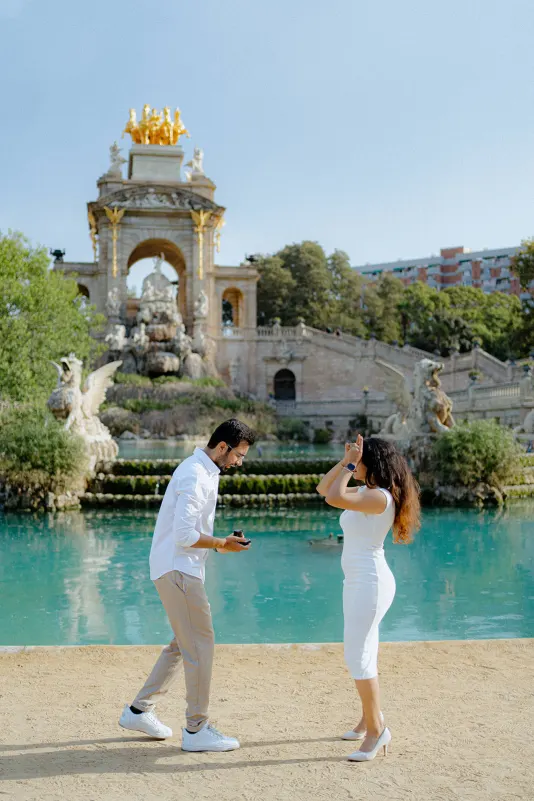 A man proposes to his surprised partner beside the fountain at Parc de la Ciutadella during a surprise proposal photoshoot.