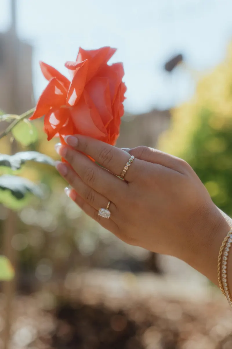 A newly engaged hand with a sparkling ring gently holds a rose, captured during a surprise proposal photoshoot.