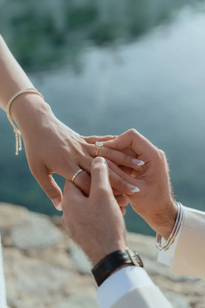 A romantic lakeside surprise proposal as he gently slides an engagement ring onto her hand.