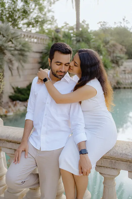 A woman embraces her partner and kisses his cheek by the water during a surprise proposal photoshoot in Barcelona.