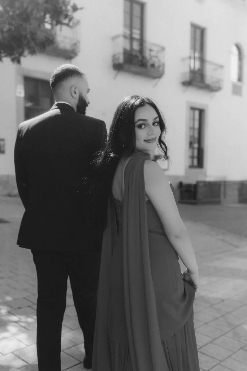 A woman in a flowing red dress glances back with a smile during a surprise proposal photoshoot outdoors.