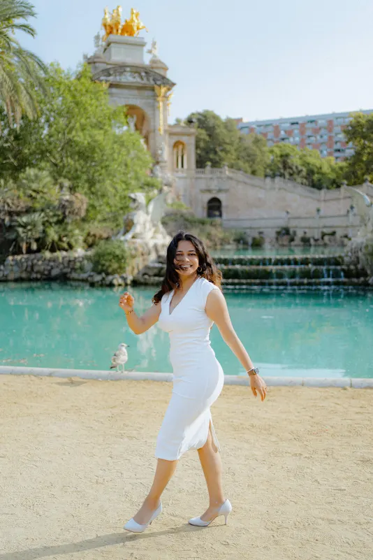 A woman in a white dress beams with excitement by the fountain at Parc de la Ciutadella during a surprise proposal shoot.
