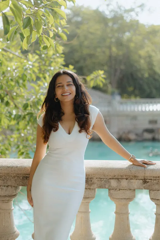 A woman in a white dress smiles radiantly by the turquoise water during a surprise proposal photoshoot in Barcelona.