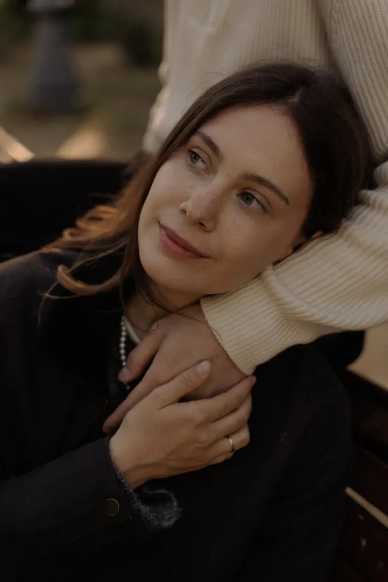 A woman leans into her partner’s embrace on a park bench, sharing a peaceful moment during a couples & engagements shoot.