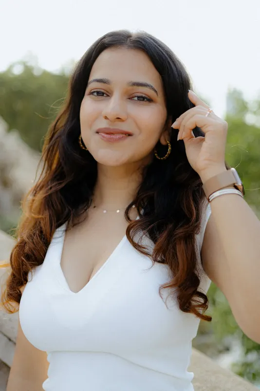 A woman smiles softly in the sunlight, showing her engagement ring during a surprise proposal photoshoot in the park.