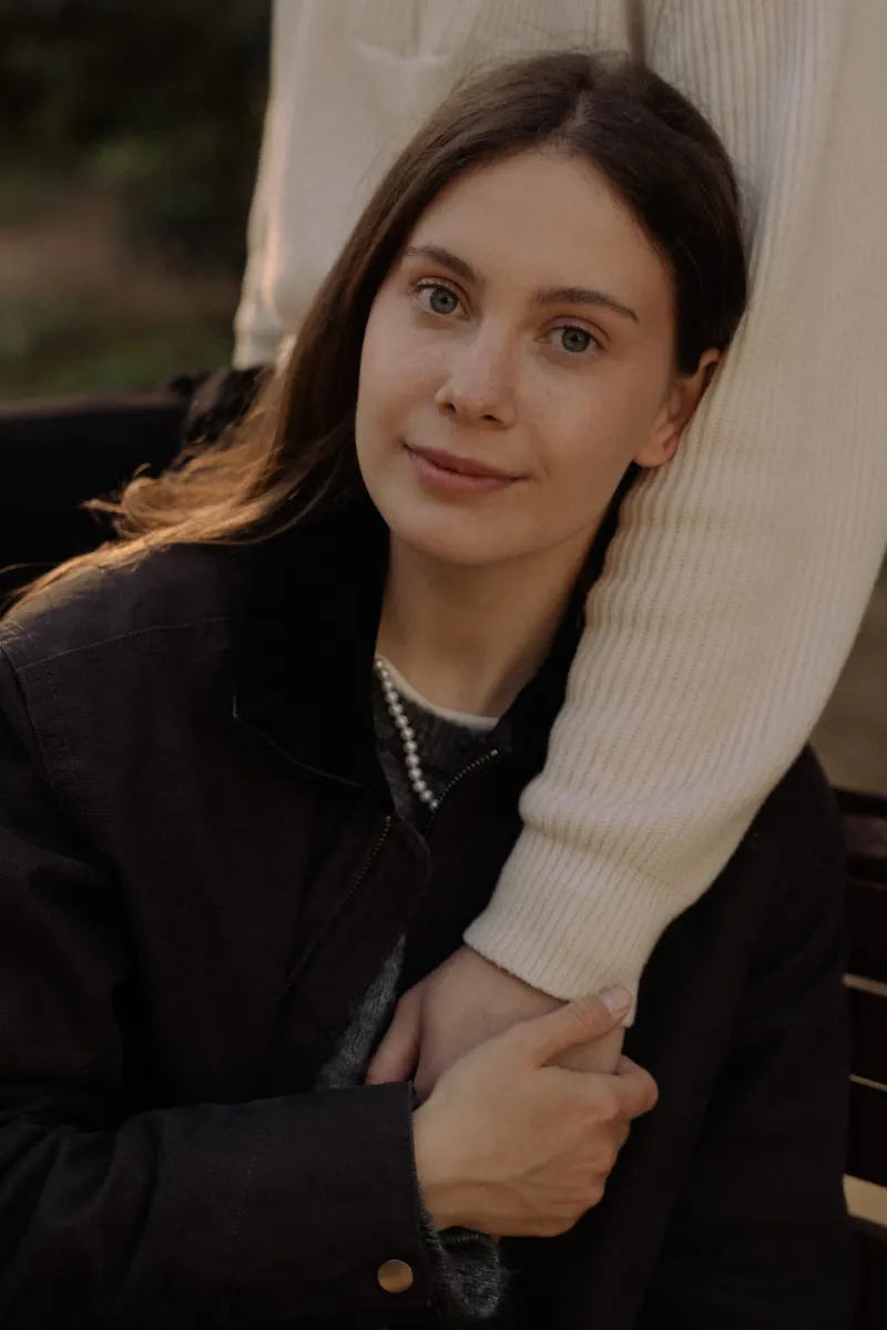 A woman smiles softly while holding her partner’s arm during a cozy couples & engagements photoshoot in Barcelona.