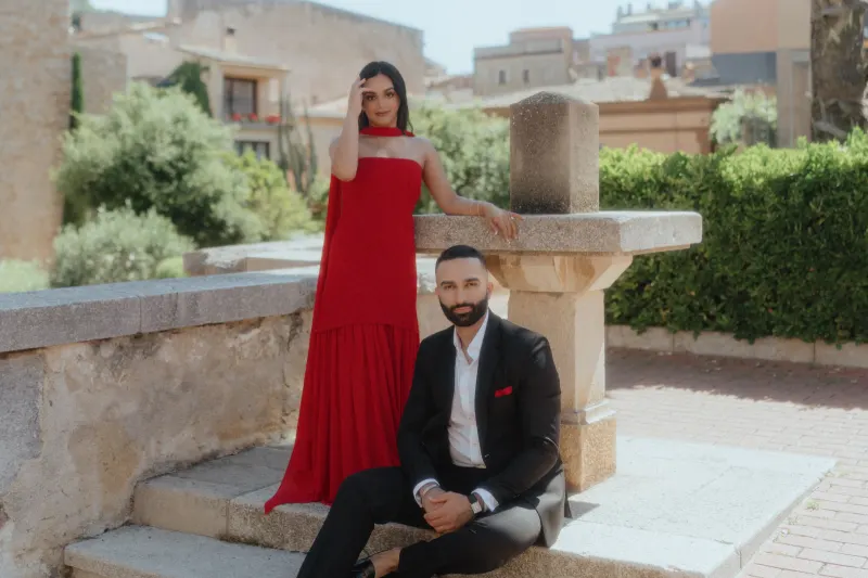 An elegant couple in Begur poses by a stone fountain, celebrating their surprise proposal with joyful expressions.