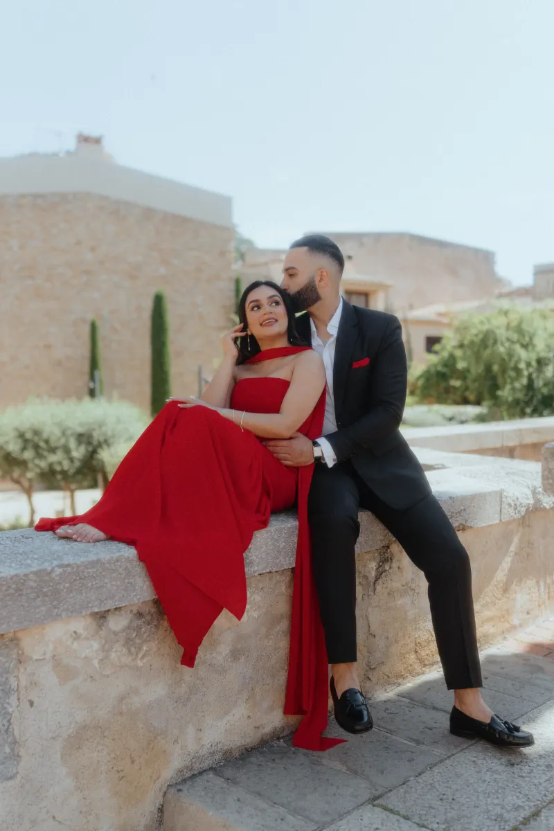 An engaged couple in formal attire share an intimate moment on a sunlit stone terrace in Begur after a surprise proposal.