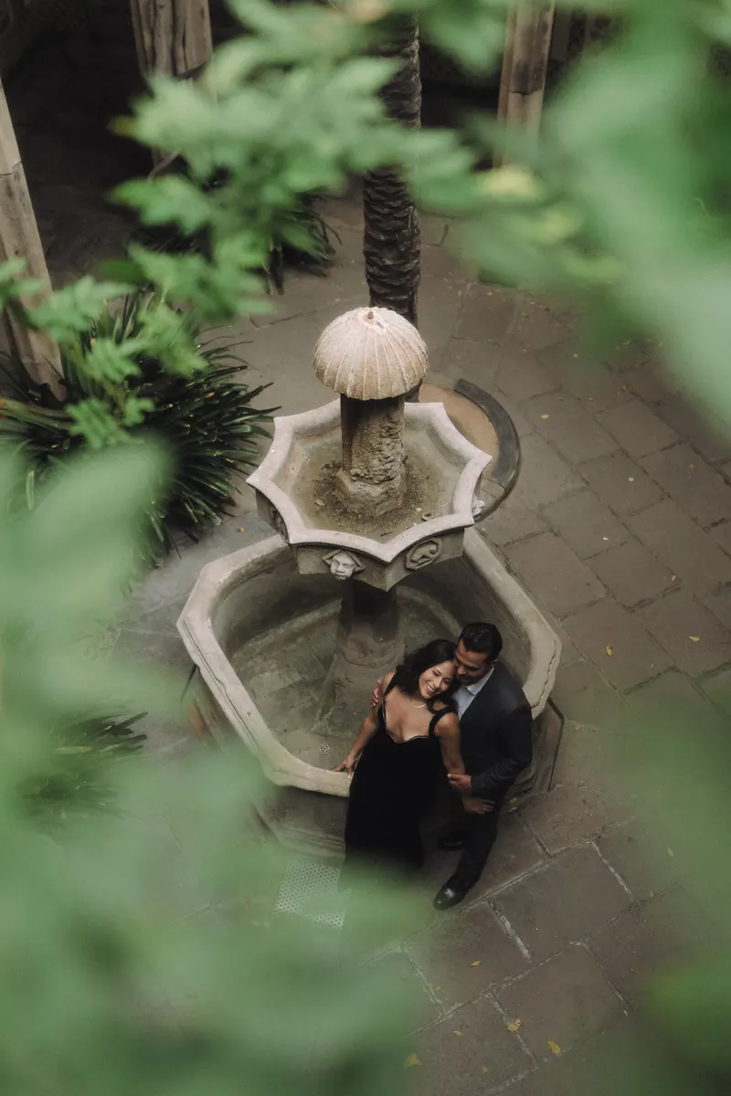 An overhead view of Ashley and Edgar beside a stone fountain surrounded by greenery.