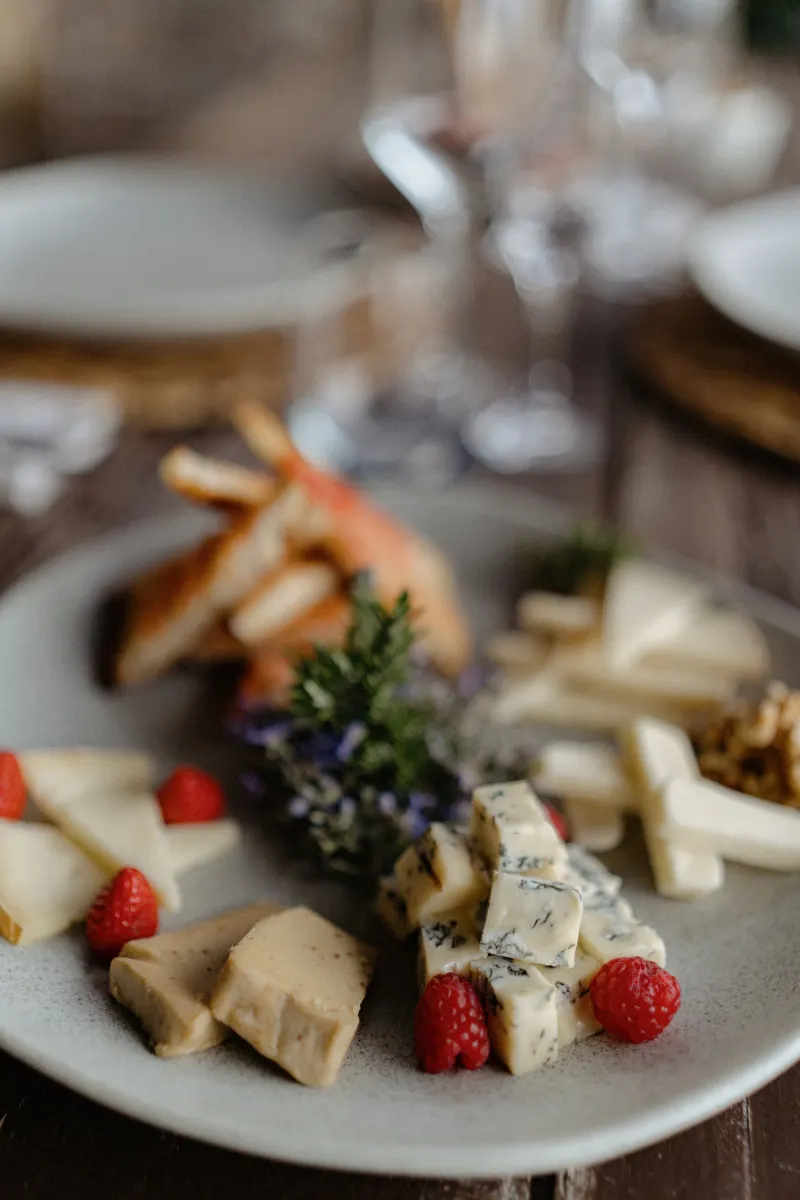 Artisan cheese platter with fresh raspberries and herbs, styled for a countryside surprise proposal photoshoot.