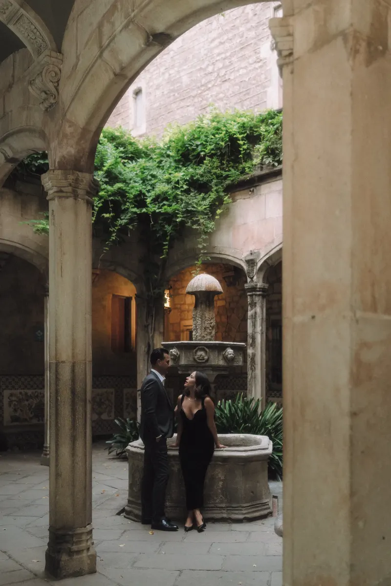 Ashley and Edgar are framed by a stone arch at the entrance to a quiet Gothic Quarter courtyard.