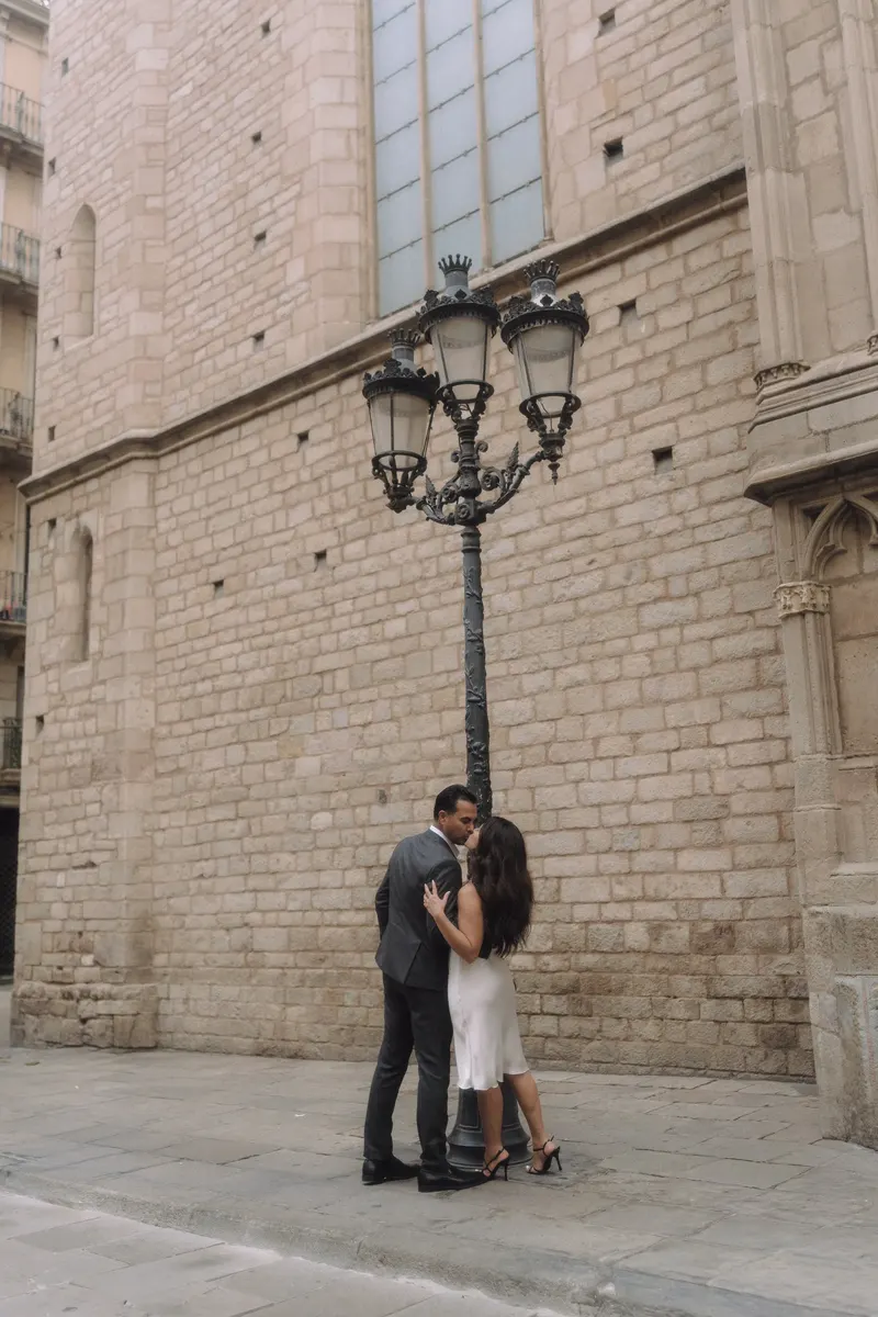 Ashley and Edgar embrace beneath ornate street lamps in a peaceful Barcelona square.
