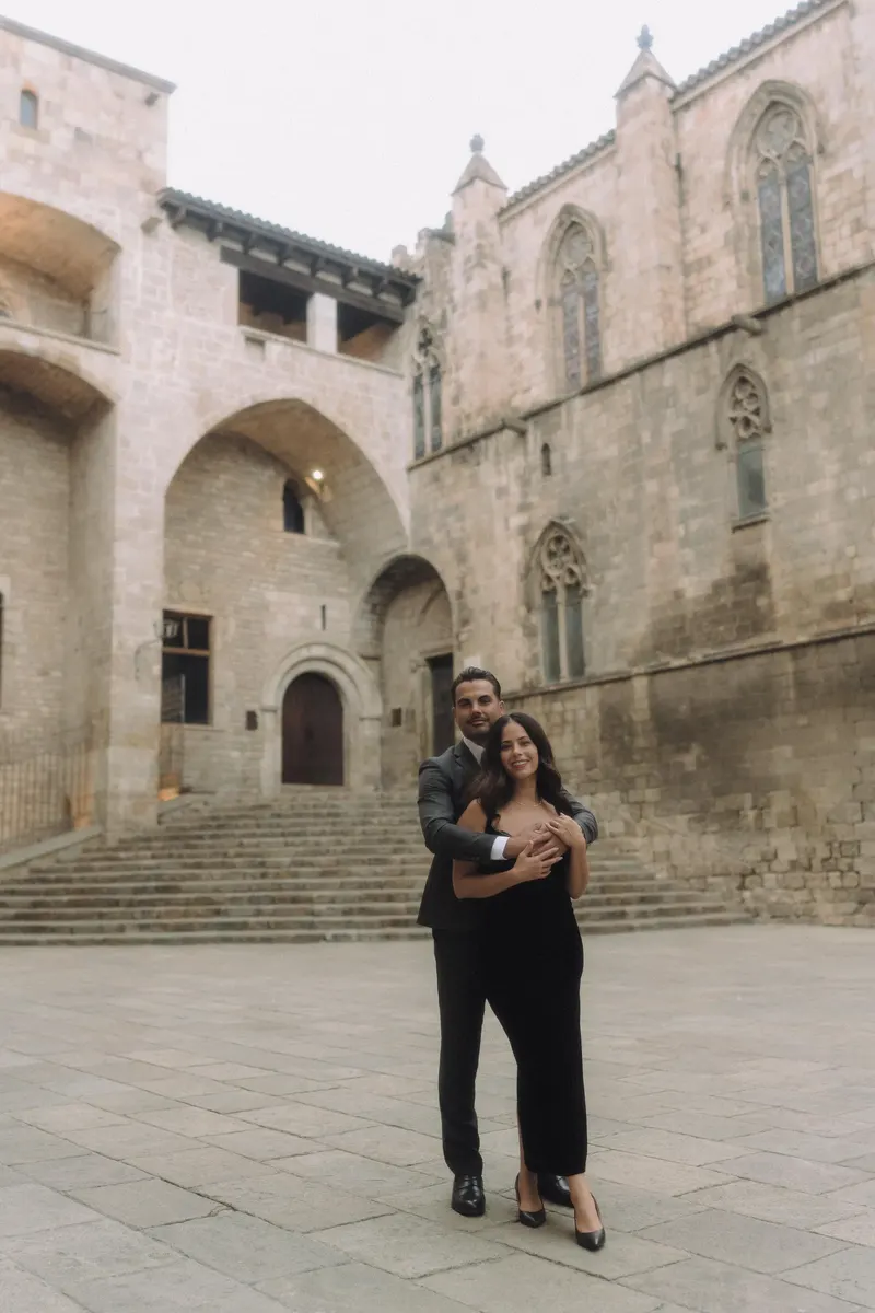 Ashley and Edgar embrace in the historic setting of Plaça del Rei.