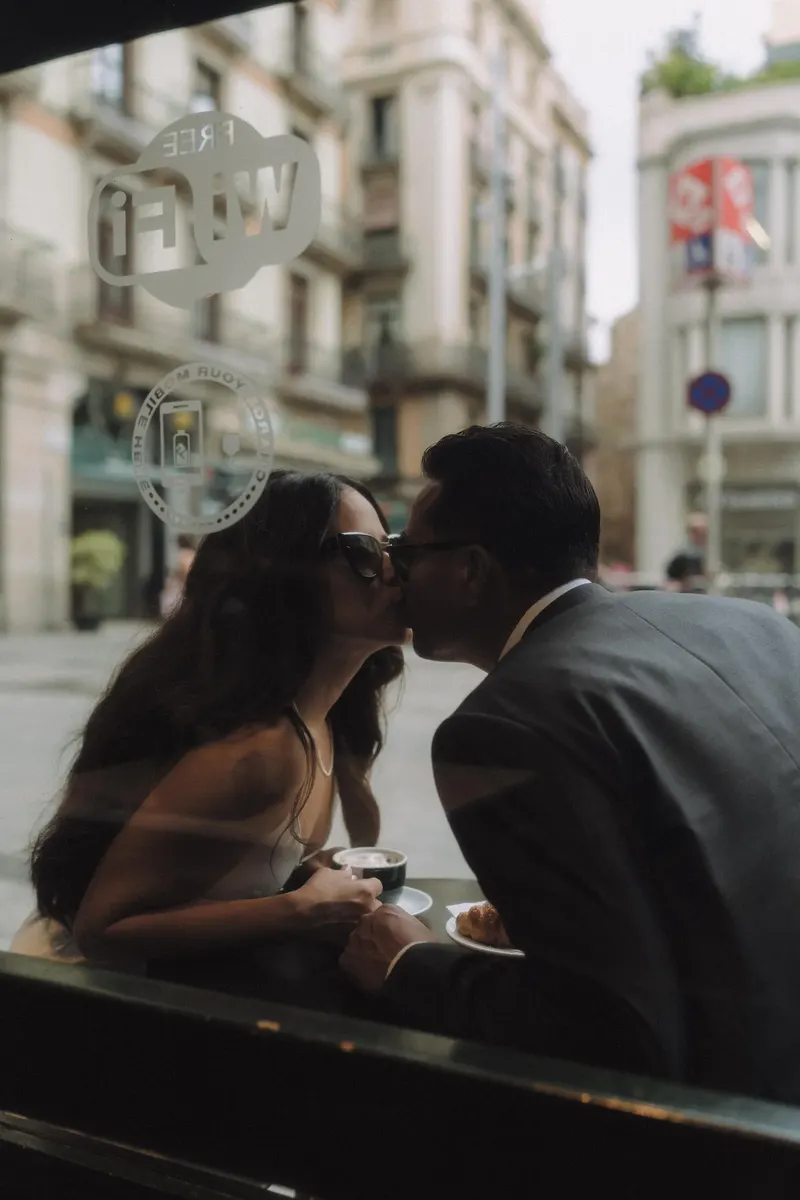 Ashley and Edgar kiss through the cafe window during their relaxed morning photoshoot.