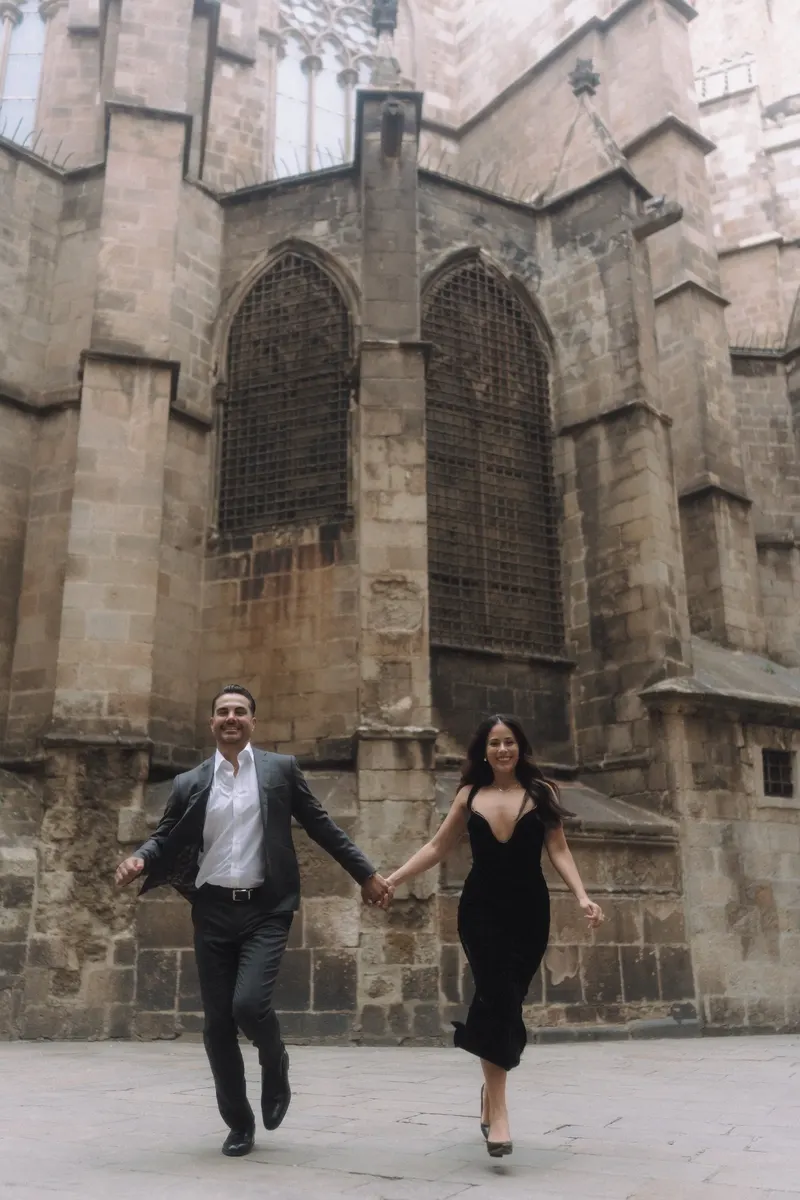 Ashley and Edgar run hand in hand past a Gothic church during their Barcelona photoshoot.