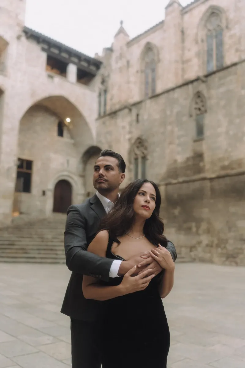 Ashley and Edgar share a close embrace against the stone architecture of Plaça del Rei.