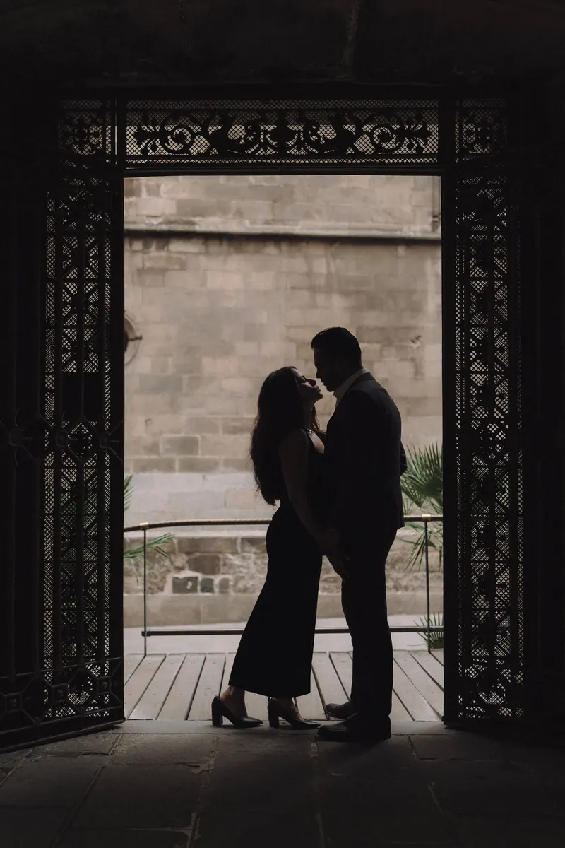 Ashley and Edgar share a kiss in silhouette beneath an ornate stone arch.