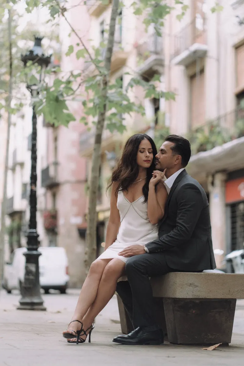 Ashley and Edgar sit close together on a stone bench beneath leafy trees.