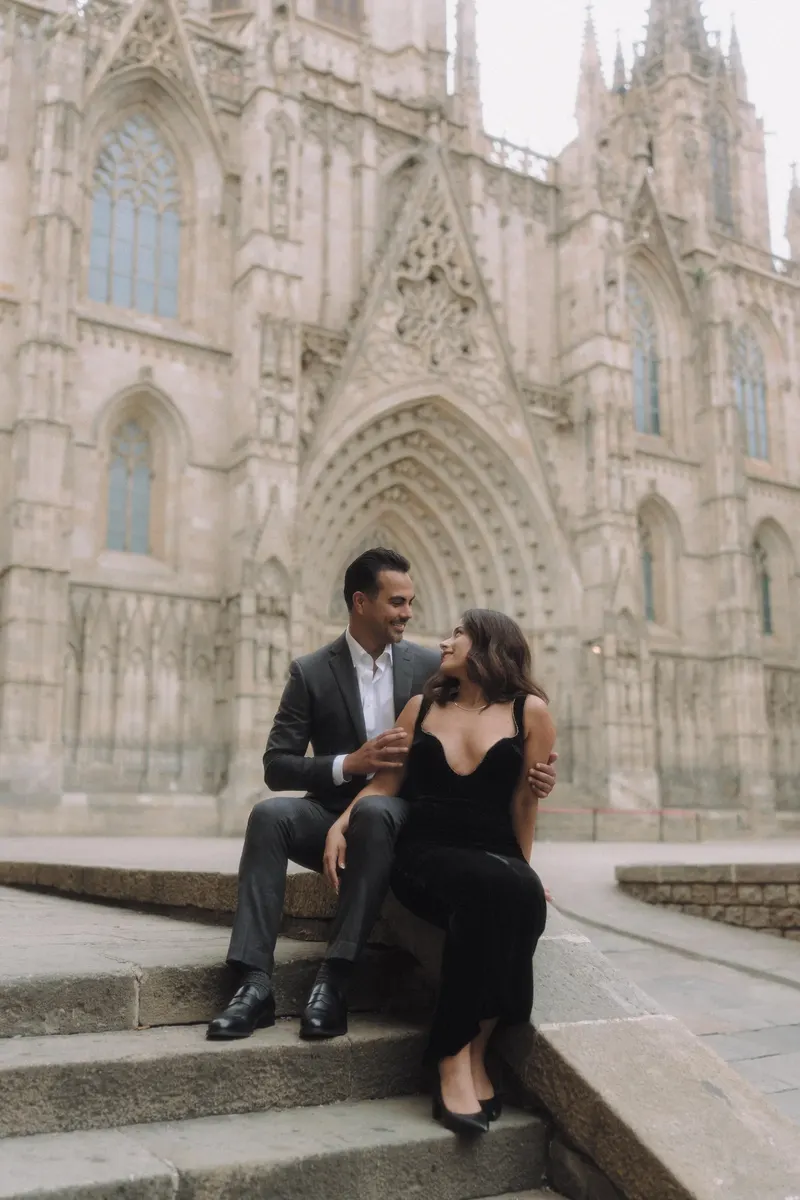 Ashley and Edgar sit close together on the stone steps beside Barcelona Cathedral.