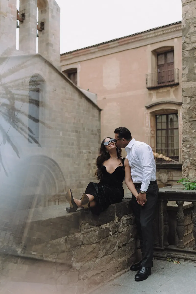 Ashley and Edgar sit together on a stone wall during their romantic walk through the Gothic Quarter.