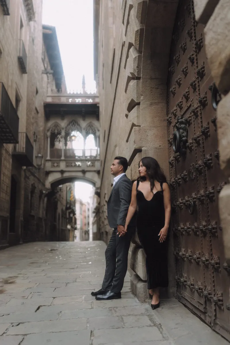 Ashley and Edgar stand beside a carved wooden doorway under Pont del Bisbe.
