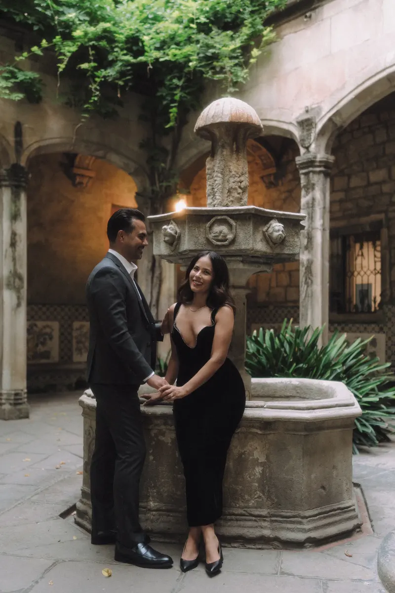 Ashley and Edgar stand beside a historic fountain in a hidden courtyard of Barcelona's Gothic Quarter.
