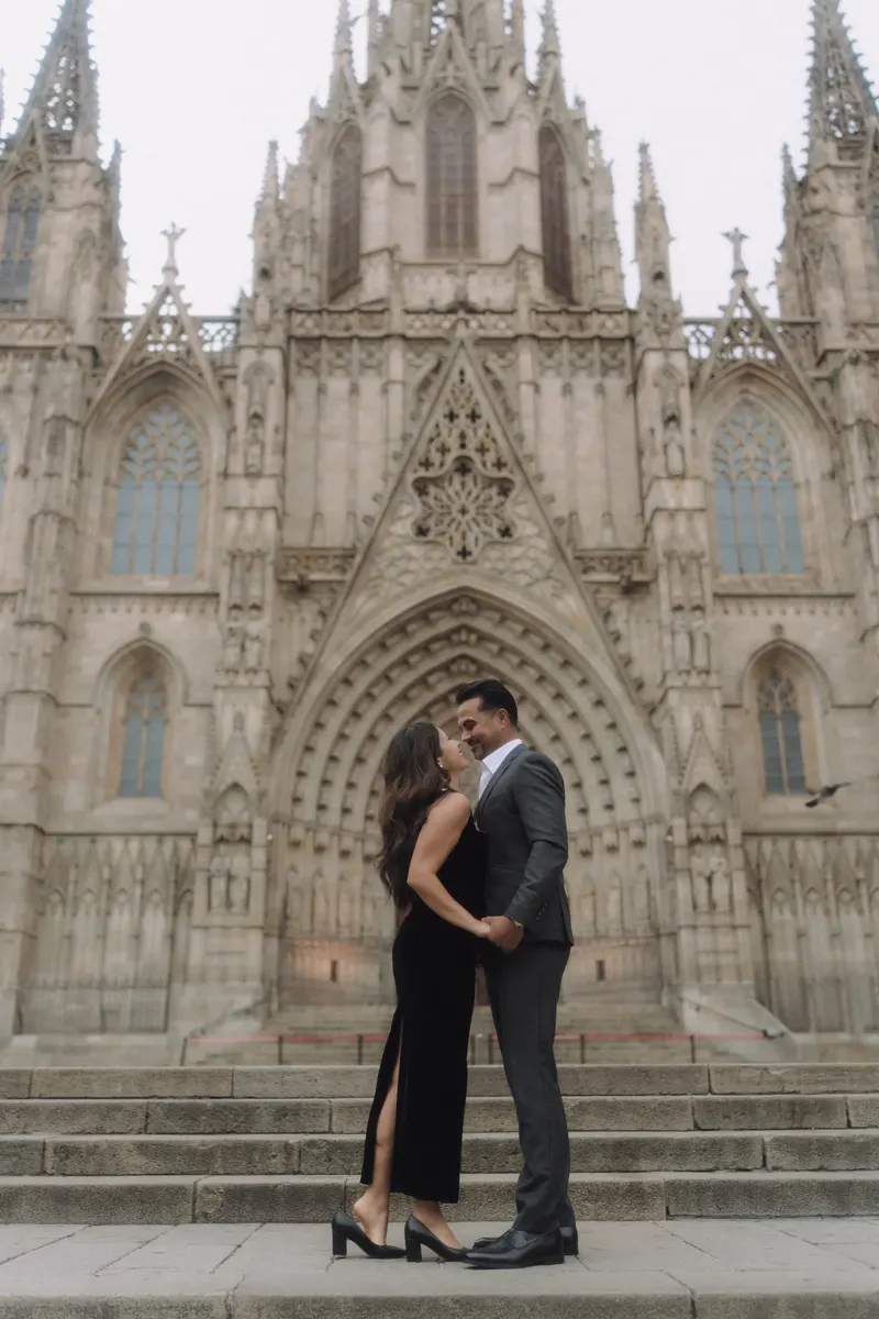 Ashley and Edgar stand face to face before the ornate facade of Barcelona Cathedral.